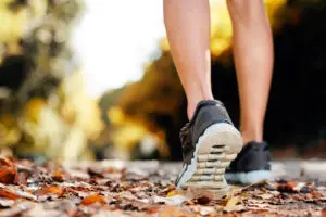 Close-up of a person's feet walking through fallen autumn leaves in athletic shoes, representing pain-free mobility and an active lifestyle after joint replacement surgery