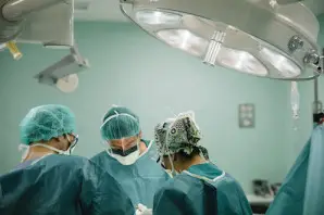 Surgical team of three focused on a procedure in a hospital operating room under large overhead surgical lights