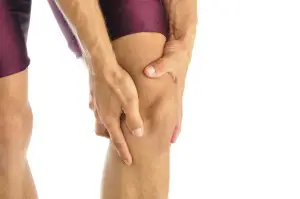 Athletic person clutching their knee with both hands against a white background, representing acute knee pain or joint discomfort