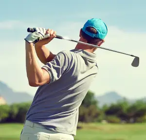 Active man completing a full golf swing on a desert golf course, viewed from behind, representing a return to recreational activity after joint replacement surgery