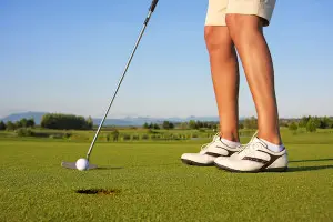 Close-up of a golfer's legs and feet lining up a putt on a green, representing pain-free mobility and an active lifestyle after joint replacement surgery