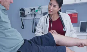Female orthopedic physician in white coat performing a knee examination on an older male patient in a hospital exam room