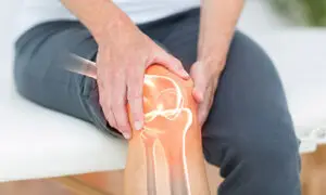 Older adult clutching their knee with a glowing x-ray overlay of the knee joint anatomy, illustrating knee arthritis pain and joint degeneration
