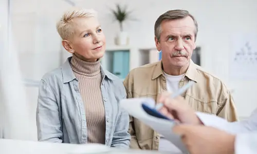 Older couple attentively listening during a medical consultation with a physician, representing a joint replacement surgical consultation visit
