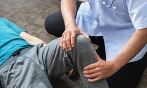 Physical therapist or clinician performing a hands-on knee assessment on a patient lying on the floor during a rehabilitation or evaluation session