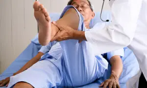Orthopedic physician performing a passive hip range of motion examination on an elderly patient lying on a clinical exam table