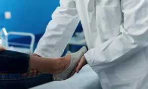 Orthopedic physician in white coat performing a hands-on ankle and foot examination on a patient in a clinical setting