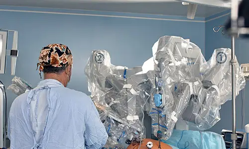 Orthopedic surgeon operating a robotic surgical system in a modern hospital operating room, viewed from behind