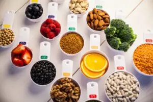 Overhead flat lay of colorful nutrient-rich whole foods in measuring cups including berries, nuts, legumes, vegetables, and citrus, representing a healthy pre- and post-surgical diet