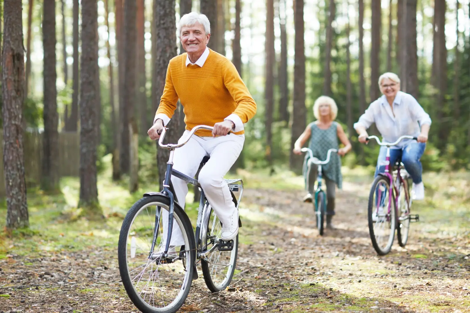Group of active seniors riding bicycles together along a forested trail, smiling and enjoying an active outdoor lifestyle after joint replacement surgery