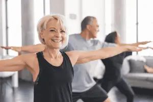 Alt Text: Active senior woman smiling while practicing yoga in a fitness class, representing a return to flexibility and active living after hip or knee replacement surgery with Dr. Brandon Gough in Scottsdale Arizona