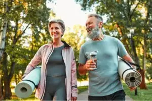 Active senior couple walking through a park carrying yoga mats, representing a return to fitness and active living after hip or knee replacement surgery with Dr. Brandon Gough in Scottsdale Arizona