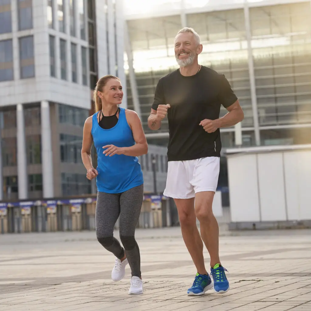 Active middle-aged couple jogging together outdoors in an urban setting, smiling and enjoying exercise after joint replacement surgery
